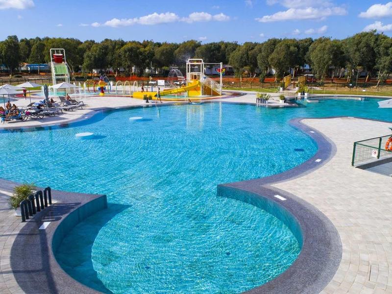 Grand bassin extérieur avec toboggans et zones de détente sous un ciel ensoleillé.