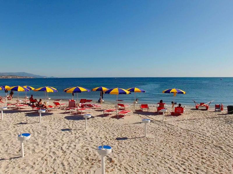 Plage avec parasols jaune-bleu et chaises rouges au bord de la mer sous un ciel clair.