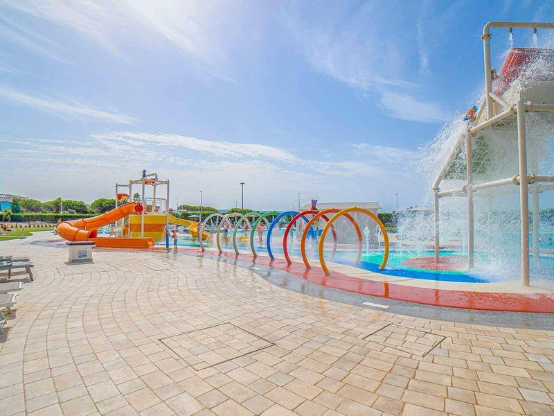 Parc aquatique extérieur avec toboggans, fontaines et chaises longues sous un ciel clair.