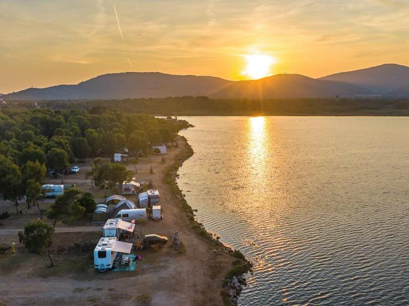 Coucher de soleil sur un lac avec des camping-cars et des arbres le long du rivage