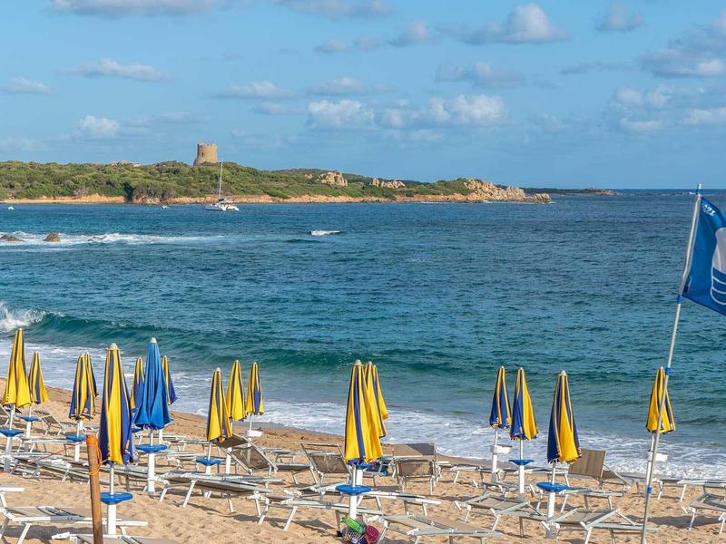 Strand mit gelben und blauen Sonnenschirmen und Blick auf das Meer und eine Insel im Hintergrund.