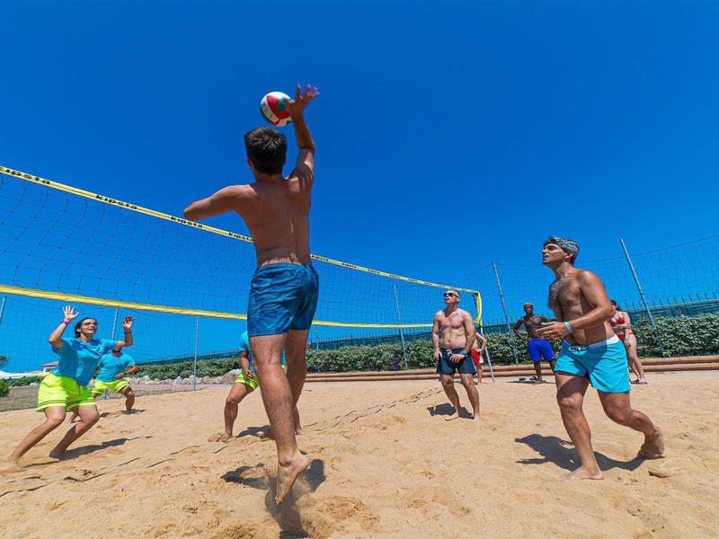 Gruppe spielt Beachvolleyball auf sandigem Strand bei strahlend blauem Himmel.