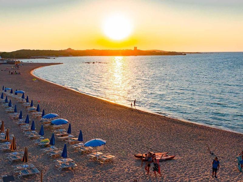 Strand mit Reihen von Sonnenschirmen und Liegestühlen bei Sonnenuntergang am Meer.
