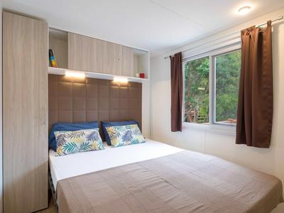 Příjemná ložnice s velkými okny, manželskou postelí a skříní v neutrálních barvách.