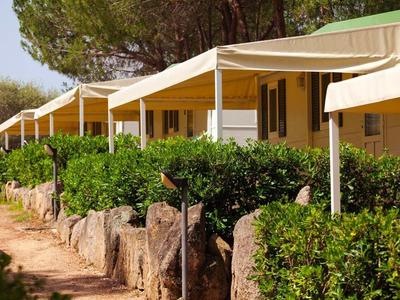 Řada bungalovů s bílými slunečními stříškami a zelenými keři vpředu