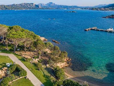 Pohled na pobřeží se zelenou zahradou, stromy a modrým mořem za slunečného dne.