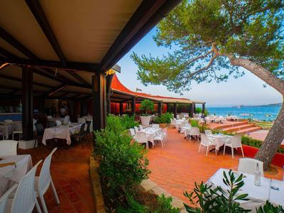 Buitenterras van een restaurant met witte tafels en stoelen, uitzicht op zee in de avond.