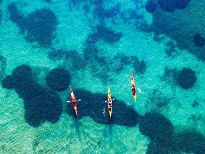 Drie kajaks varen op helder turquoise water boven een zeebodem met donkere algenplekken.