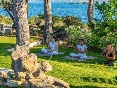 Vier mensen doen yoga buiten op een groen grasveld met uitzicht op zee.