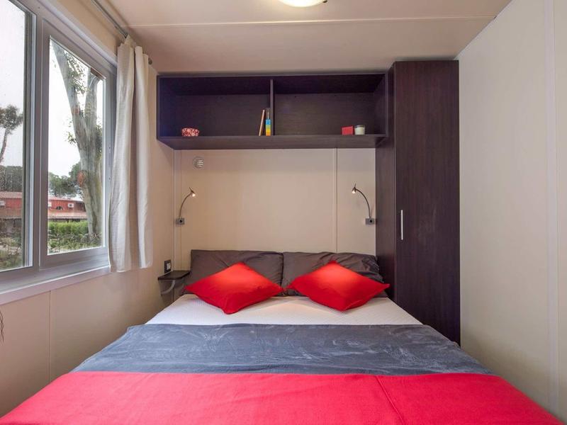 Kompaktní ložnice s manželskou postelí, červenými polštáři a velkým oknem.