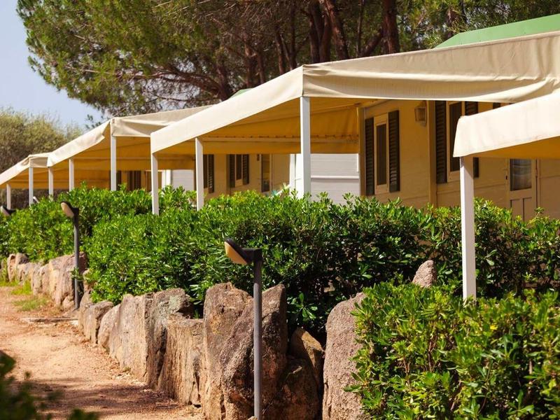 Řada bungalovů s bílými slunečními stříškami a zelenými keři vpředu