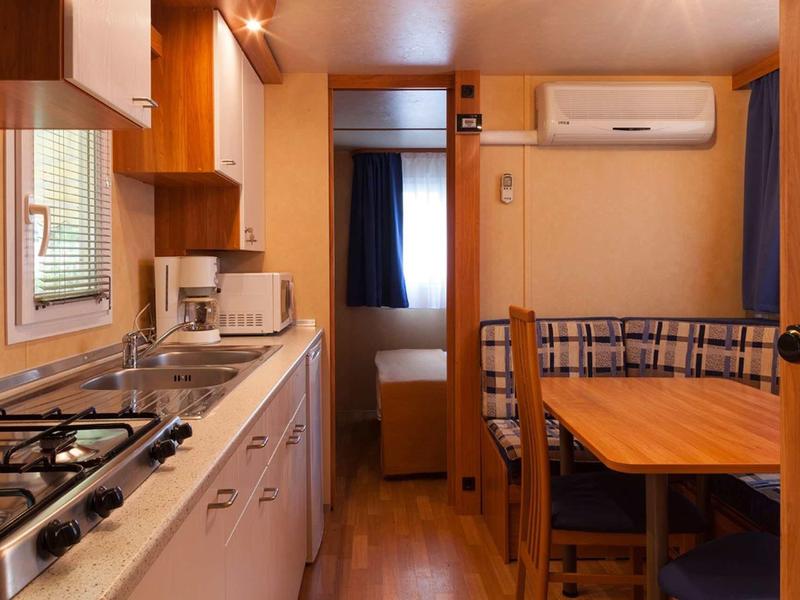 Příjemný interiér rekreačního domu s kuchyní, jídelním stolem a spací částí v pozadí.