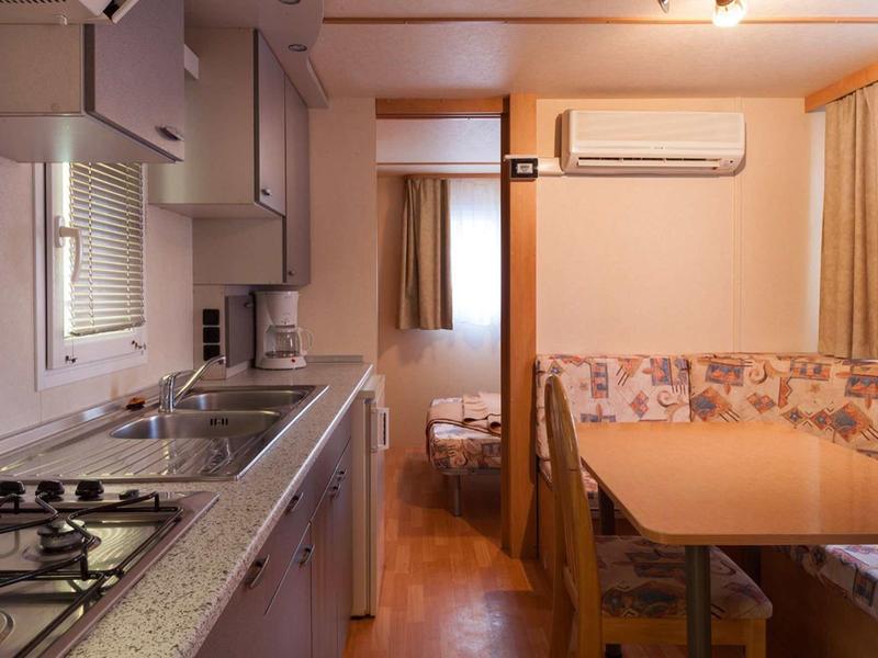 Malá kuchyňka s plynovým sporákem a jídelním koutem v rekreačním domě nebo karavanu.