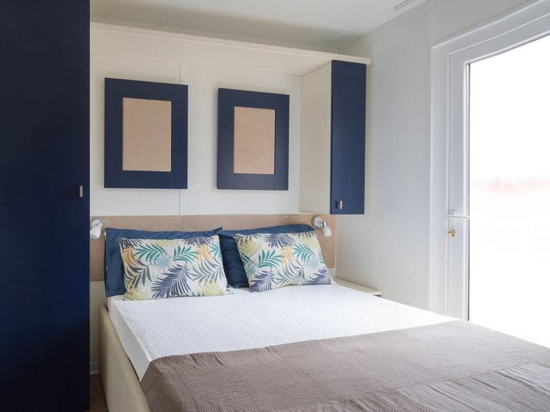 Pohodlná postel s modrými skříněmi a velkými okny v moderním hotelovém pokoji.