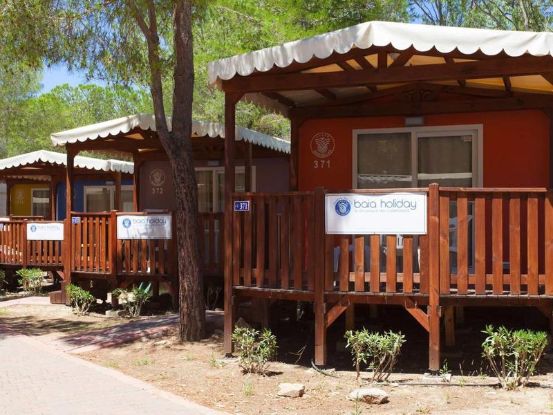 Řada malých dřevěných chat se verandami v zastíněné lesnaté rekreační oblasti.