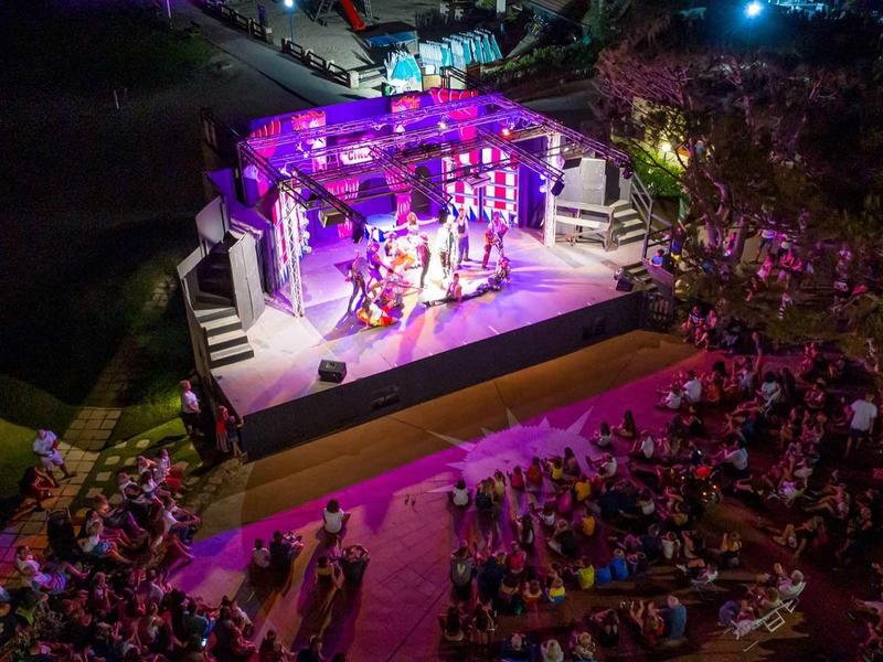 Večerní živé vystoupení na osvětleném venkovním pódiu před velkým publikem.