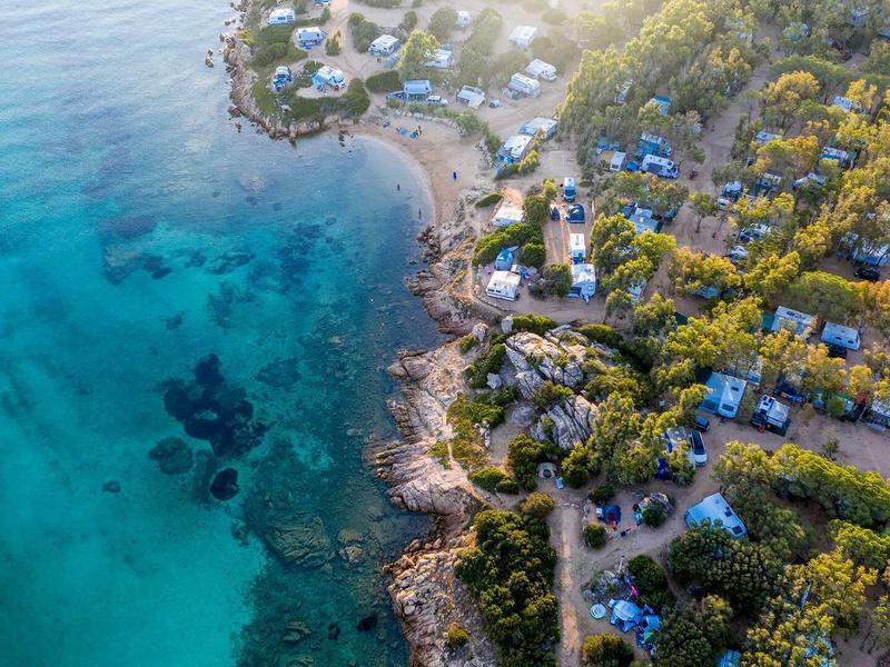 Letecký pohled na pobřeží s čistou tyrkysovou vodou a hotelovým komplexem obklopeným stromy.