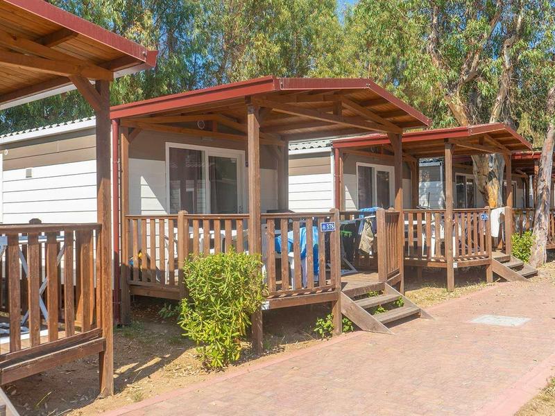 Řada dřevěných chatek s verandami na slunném rekreačním areálu s stromy v pozadí