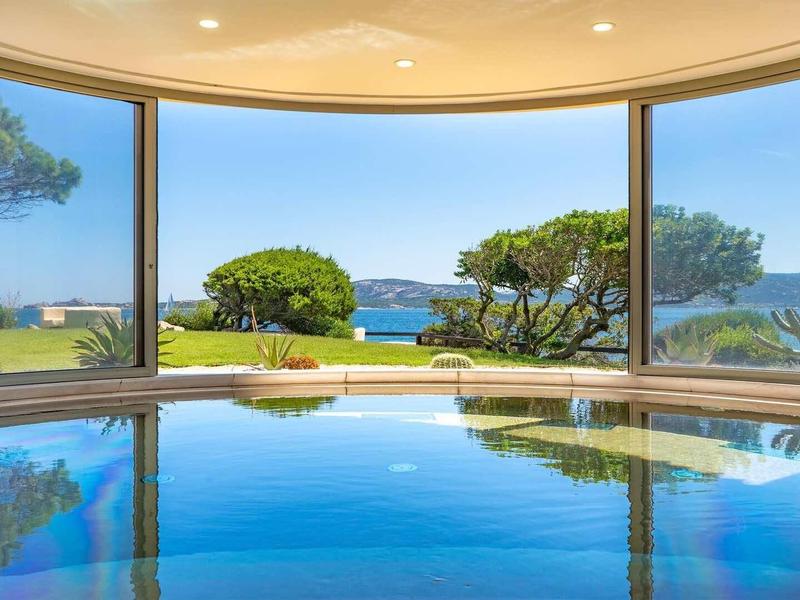 Vnitřní bazén s panoramatickým výhledem na zahradu a moře přes velká okna.