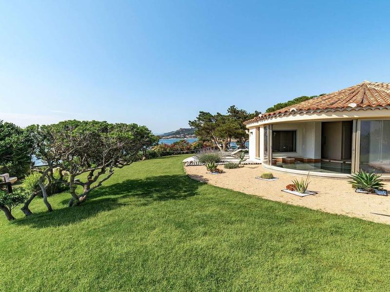 Moderní rekreační dům s terasou a výhledem na zahradu a moře za slunečného dne.