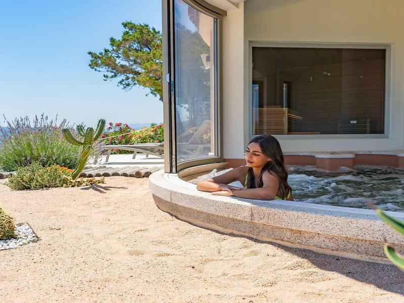 Žena relaxuje ve vířivce s výhledem na pláž a modrou oblohu v pozadí.