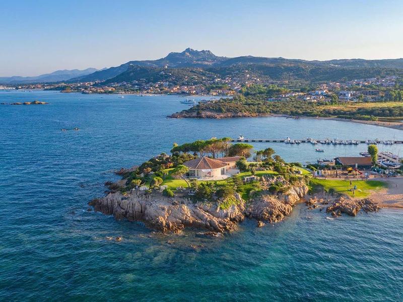 Pobřežní krajina s čistou modrou vodou, malými ostrovy a horami v pozadí.