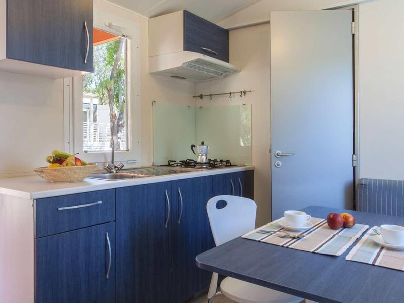 Piccola cucina con mobili blu, tavolo e sedie in una stanza luminosa.