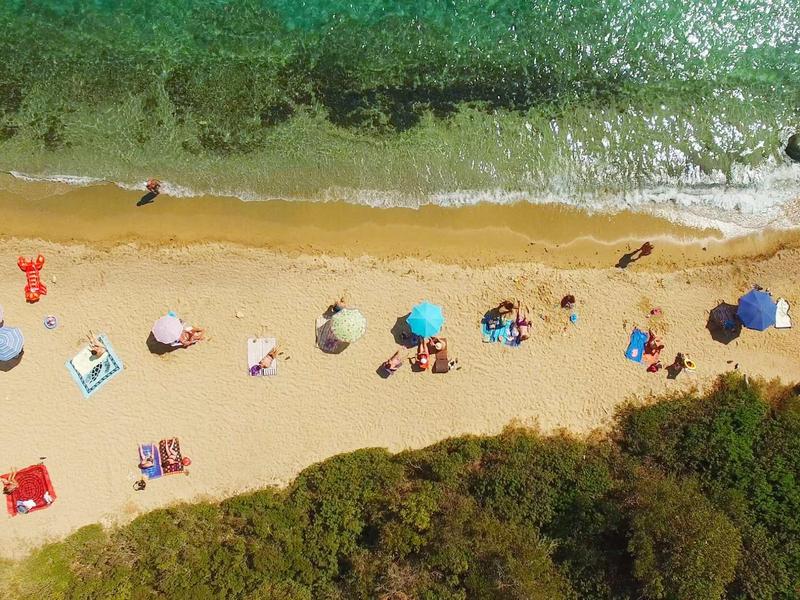 Vista aerea di una spiaggia con ombrelloni, persone e acqua verde sulla riva.