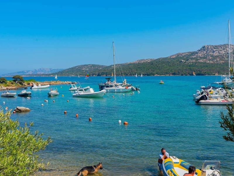Mare blu chiaro con piccole barche e persone che nuotano in una giornata di sole.