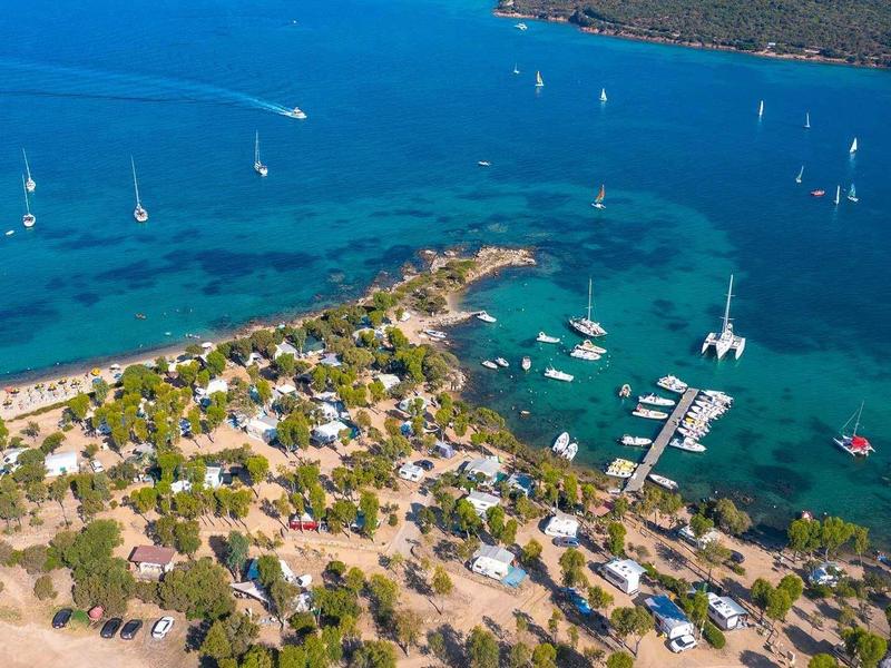 Vista aerea di una città costiera con porto turistico e barche a vela nel mare azzurro.