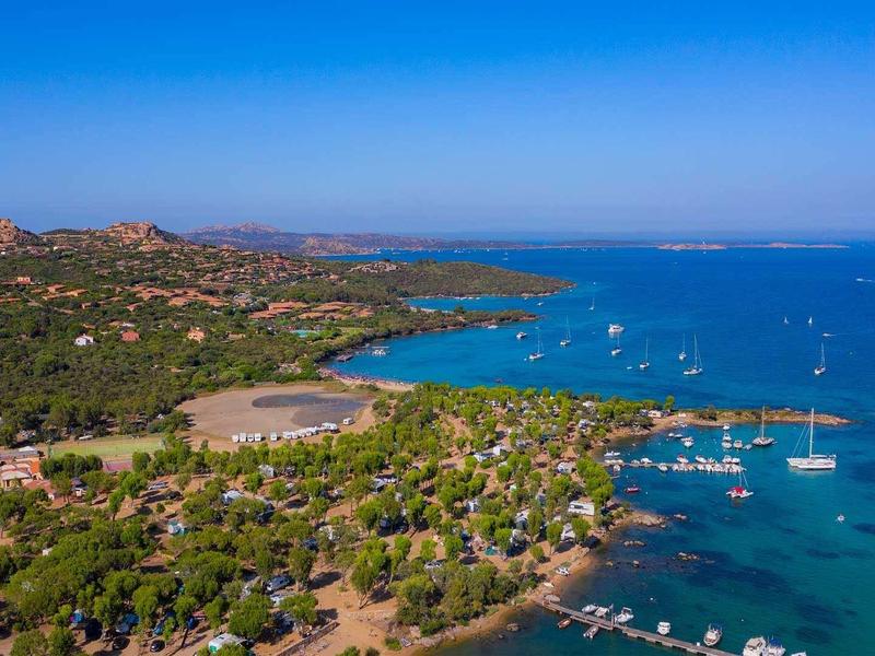 Veduta di un paesaggio costiero con mare blu, barche e colline boschive sotto un cielo limpido.