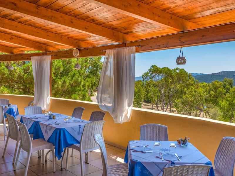 Terrazza coperta con tavoli apparecchiati in blu e vista su colline verdi.