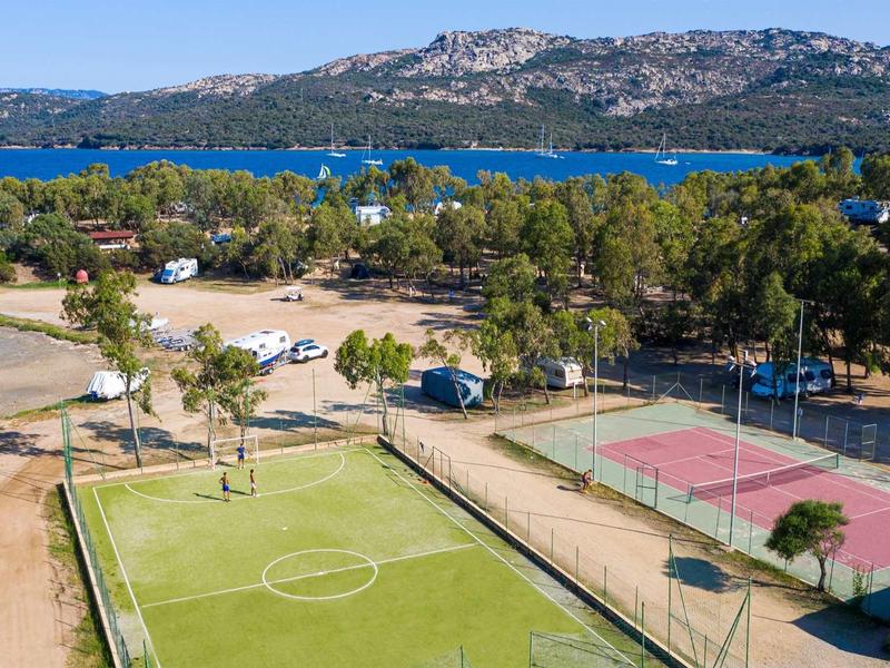 Area ricreativa con campo da calcio e campi da tennis vicino a un lago e colline boschive.
