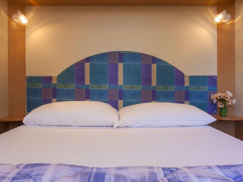 Un letto matrimoniale ben rifatto con una testiera colorata e comodini in una camera d'hotel.