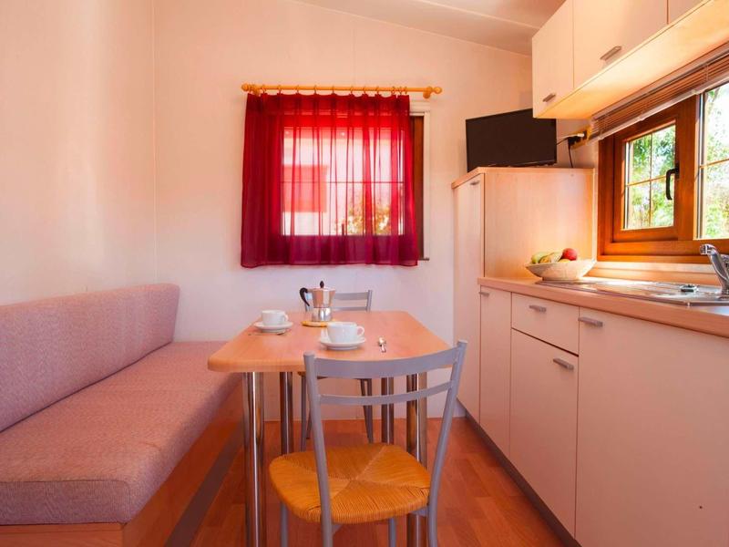 Accogliente angolo cottura con tavolo, due sedie e divano vicino a una finestra con tenda rossa.