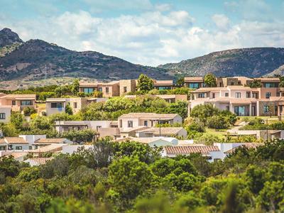 Case residenziali in un paesaggio collinare con montagne sullo sfondo sotto un cielo nuvoloso.