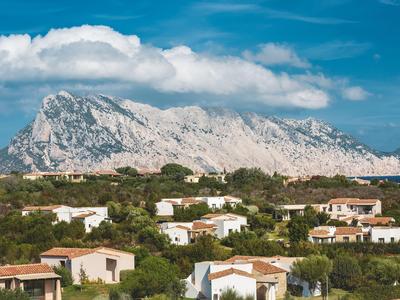 View of a holiday village with mountains in the background under a blue sky.