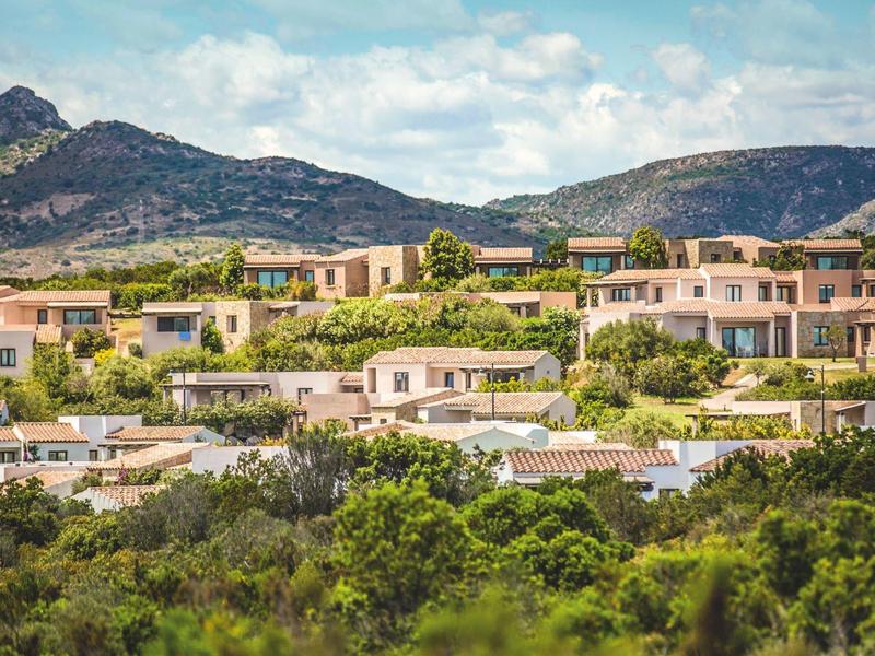 Case residenziali in un paesaggio collinare con montagne sullo sfondo sotto un cielo nuvoloso.