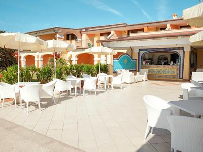 Freiluftrestaurant mit weißen Tischen und Stühlen vor einem Hotelgebäude bei klarem Himmel.