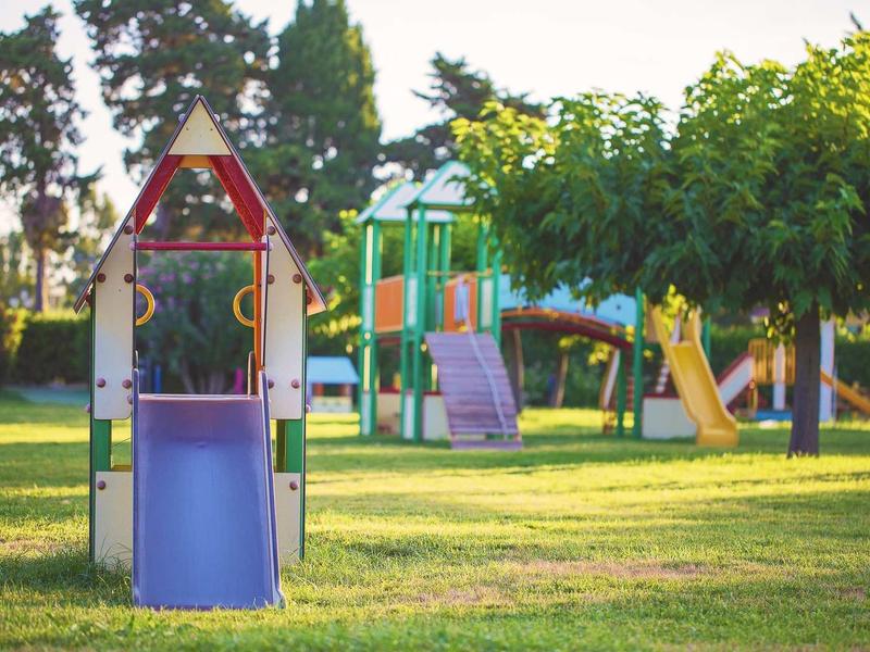 Ein bunter Kinderspielplatz mit Rutsche, Klettergerüst und grasbewachsenem Boden im Sonnenschein.