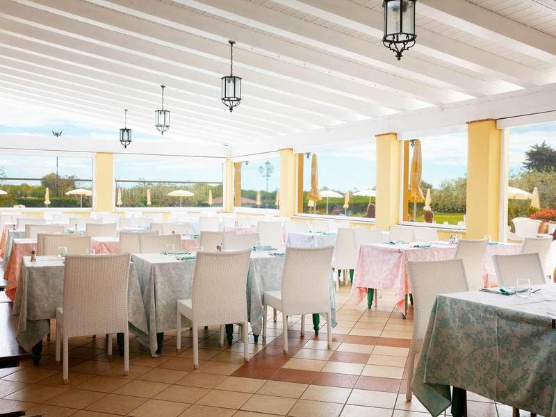 Helles, modernes Restaurant mit weißen Stühlen, Tischen und großen Fenstern mit Blick ins Grüne.