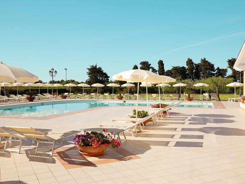 Großer Außenpool mit Liegestühlen, Sonnenschirmen und Blumendekor bei klarem Himmel.