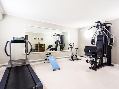 Bright gym with treadmill, workout bench, exercise bike, and multi-gym in front of large mirror.