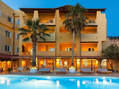 Edificio dell'hotel al crepuscolo con piscina illuminata e palme davanti.