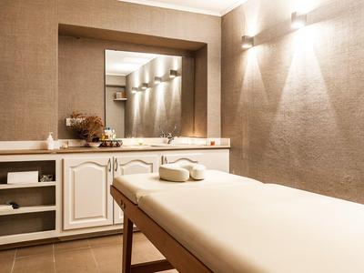 Jasny pokój do masażu z białym stołem, ręcznikami i dużym lustrem na ścianie.