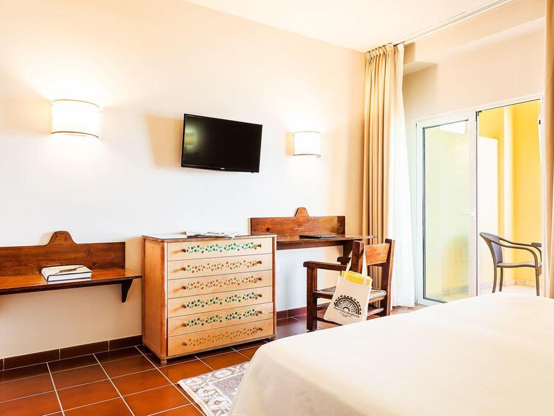 Jasny pokój hotelowy z łóżkiem, biurkiem, krzesłem, komodą, telewizorem i balkonem