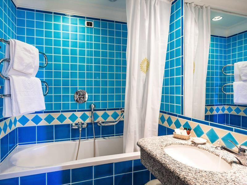 Łazienka z niebieskimi kafelkami, wanną i umywalką z lustrem.