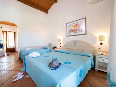 Bright hotel room with two beds, blue bedspreads, and tiled floor.