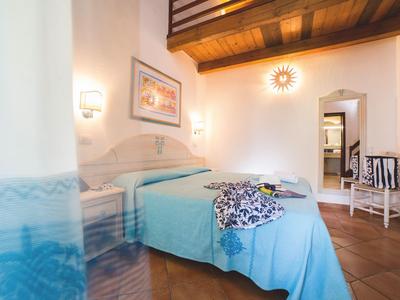 Chambre d'hôtel confortable avec lit bleu clair, plafond à poutres en bois et lumière chaude.