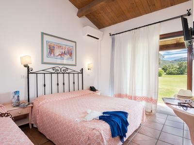 Chambre d'hôtel lumineuse avec lit double, plafond à poutres en bois, et vue sur jardin par porte coulissante.